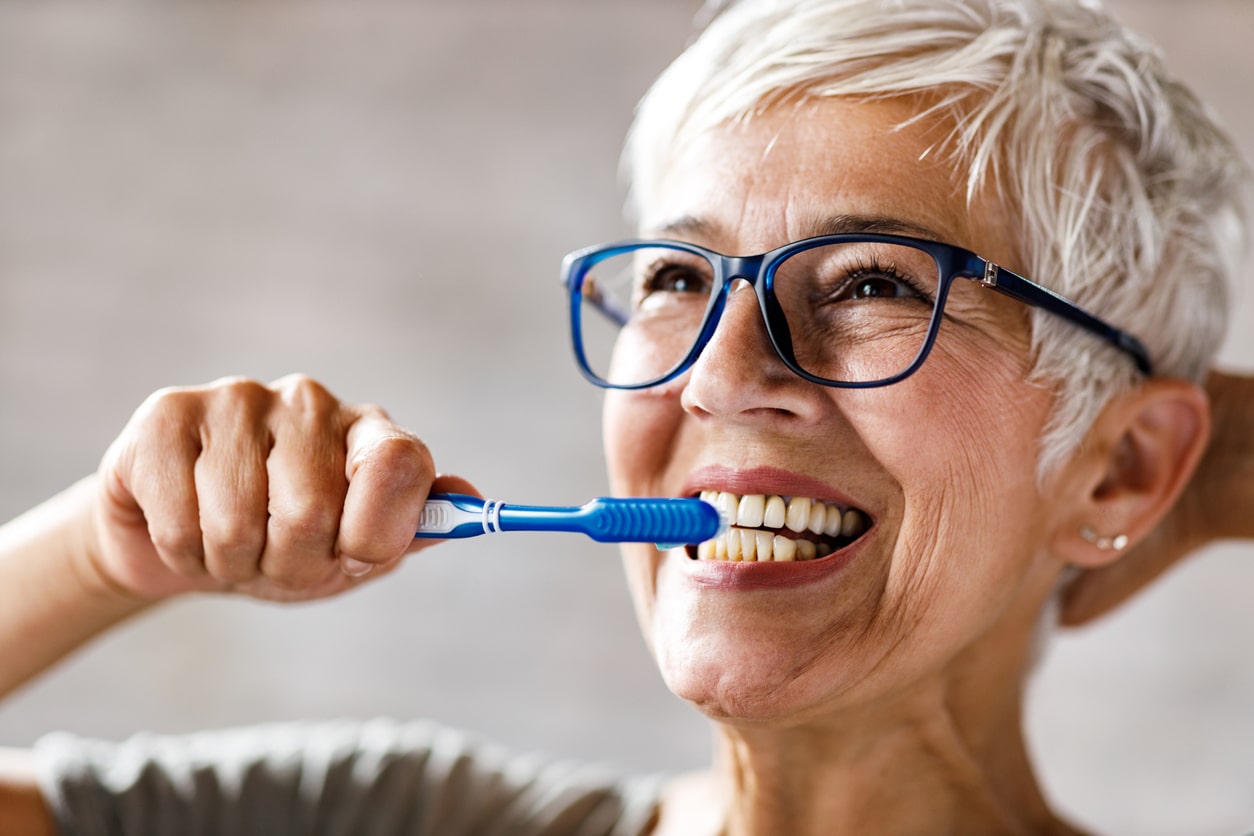 elderly woman brushing her teeth to maintain dental health for seniors