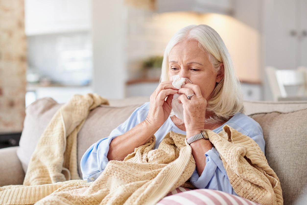 older woman sitting on her couch while blowing her nose after discovering flu questions