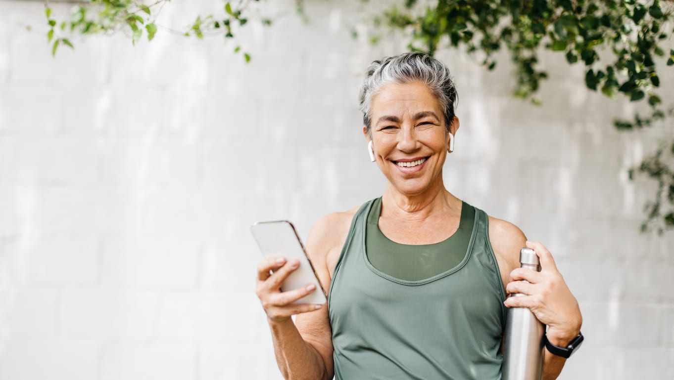 Older woman learning how to stay healthy during flu season while holding a water bottle and smiling