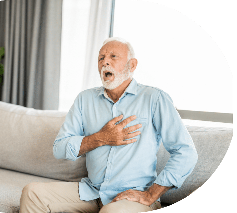 older man with white hair sitting on his couch while he holds his chest during heart failure in seniors