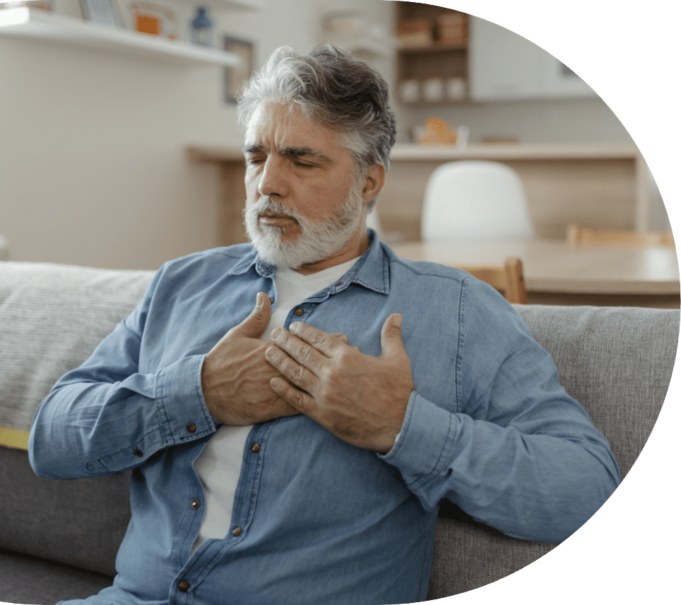 Older man sitting on the couch holding his heart due to AFib in seniors