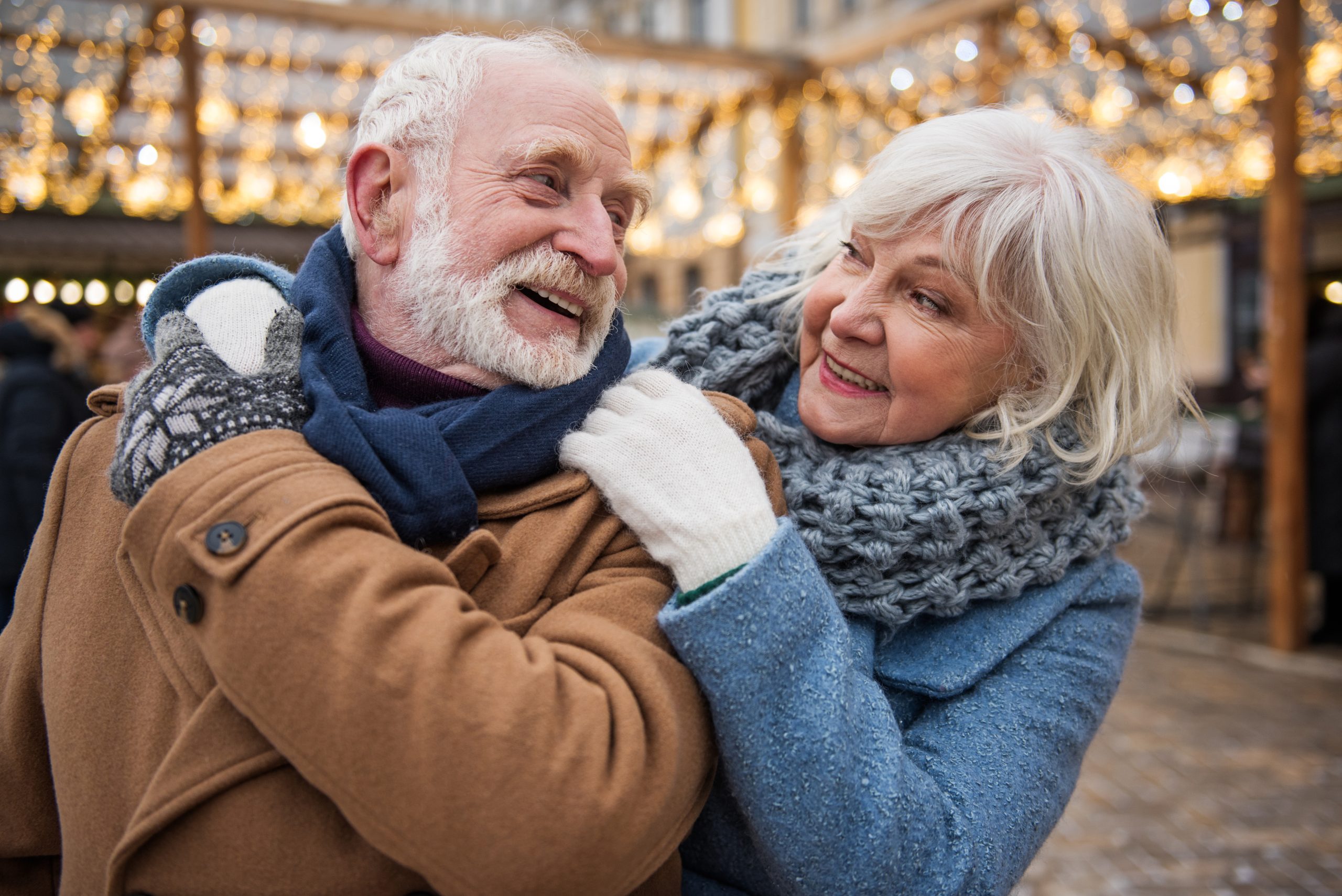 Cheerful senior woman is embracing man from behind. They are looking at each other playfully and laughing. Holiday entertainment concept